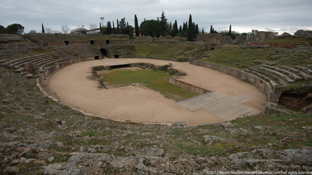 Wide elevated view of Mérida's Roman amphitheatre showing the elliptical arena, curved seating, and surrounding archaeological remains.