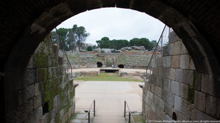 View through a dark stone arch toward the arena and opposite seating of Mérida's Roman amphitheatre.