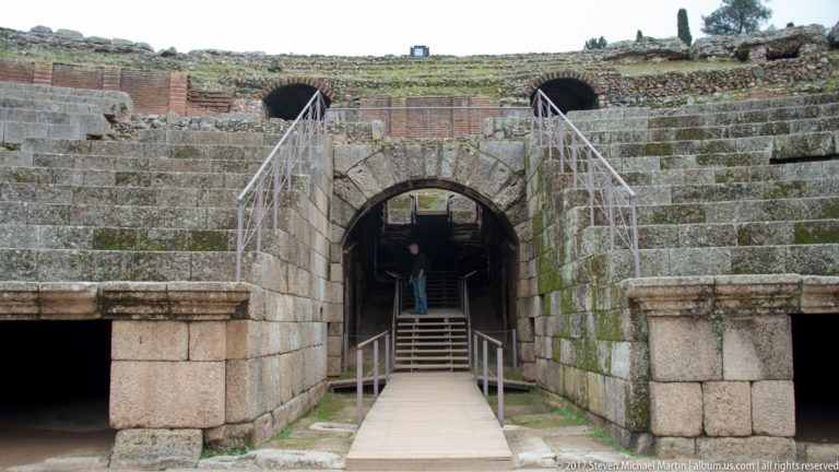 Centered stone entrance with modern stairs rising beneath the stepped seating of Mérida's Roman amphitheatre.