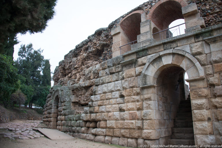 Large dressed-stone semicircular arch set into massive Roman masonry, with smaller brick arches and railing above.