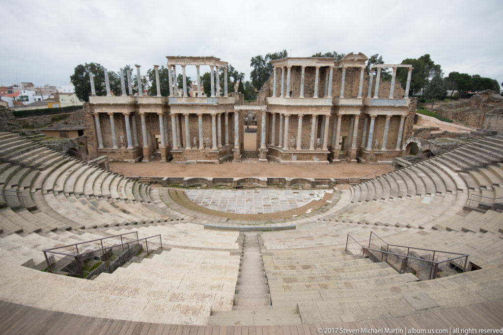 Wide elevated view of Mérida's Roman Theatre with semicircular seating, orchestra, and monumental columned stage façade.