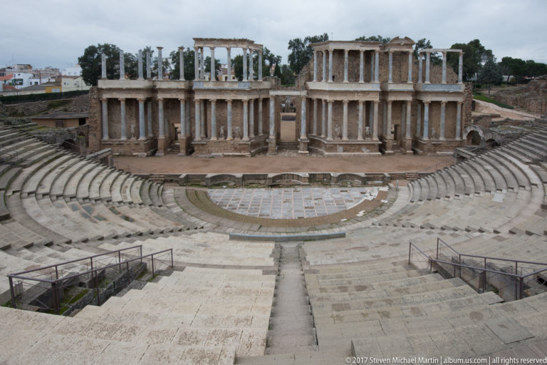 Centered elevated view of Mérida's Roman Theatre showing curved seating, orchestra, and two-story columned stage façade.