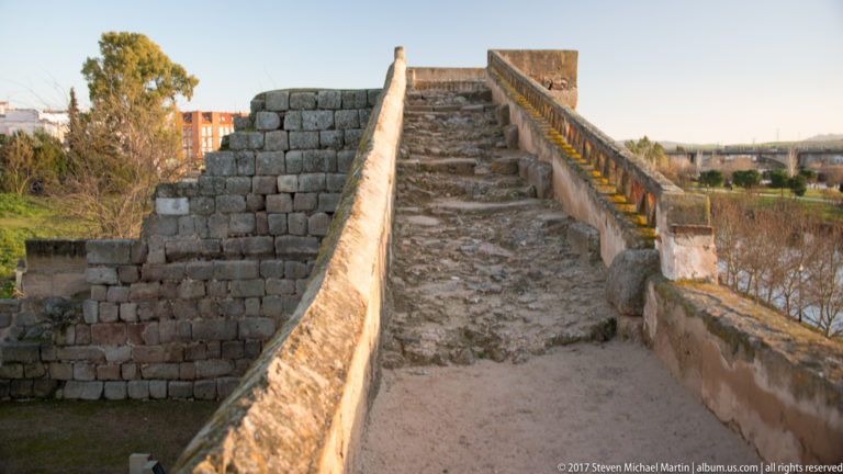Steep rough-paved passage rising between masonry parapets beside the river.