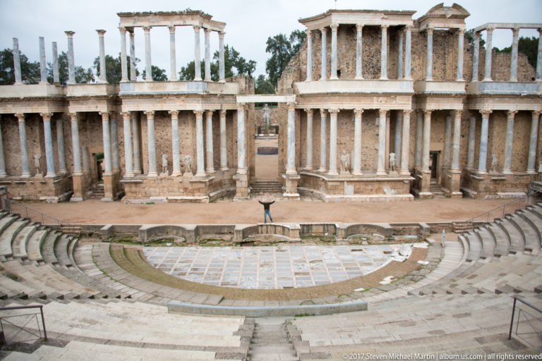 Frontal view of the tall columned scaenae frons at Mérida's Roman Theatre, with a small figure near the stage.