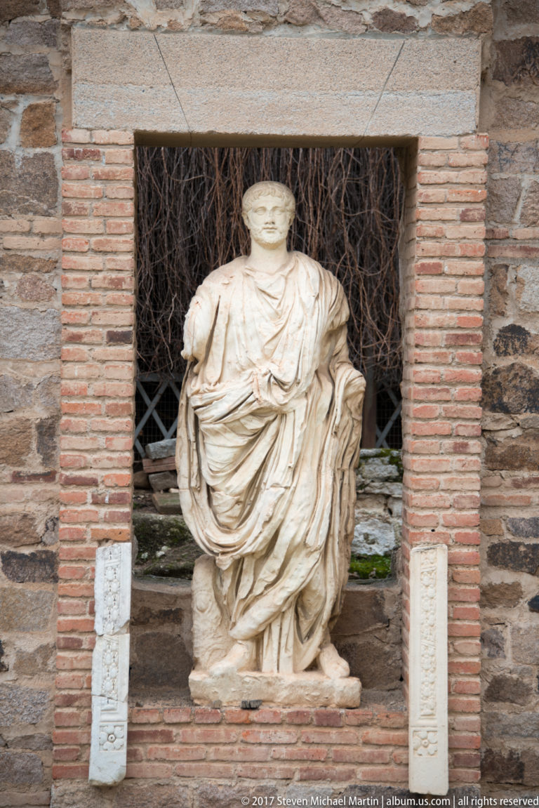 Draped female Roman statue standing in a brick-framed niche within the archaeological forum complex.