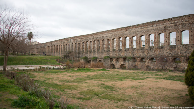 Long perspective along the tall repeating arches of Mérida's Acueducto de los Milagros beside a grassy corridor.