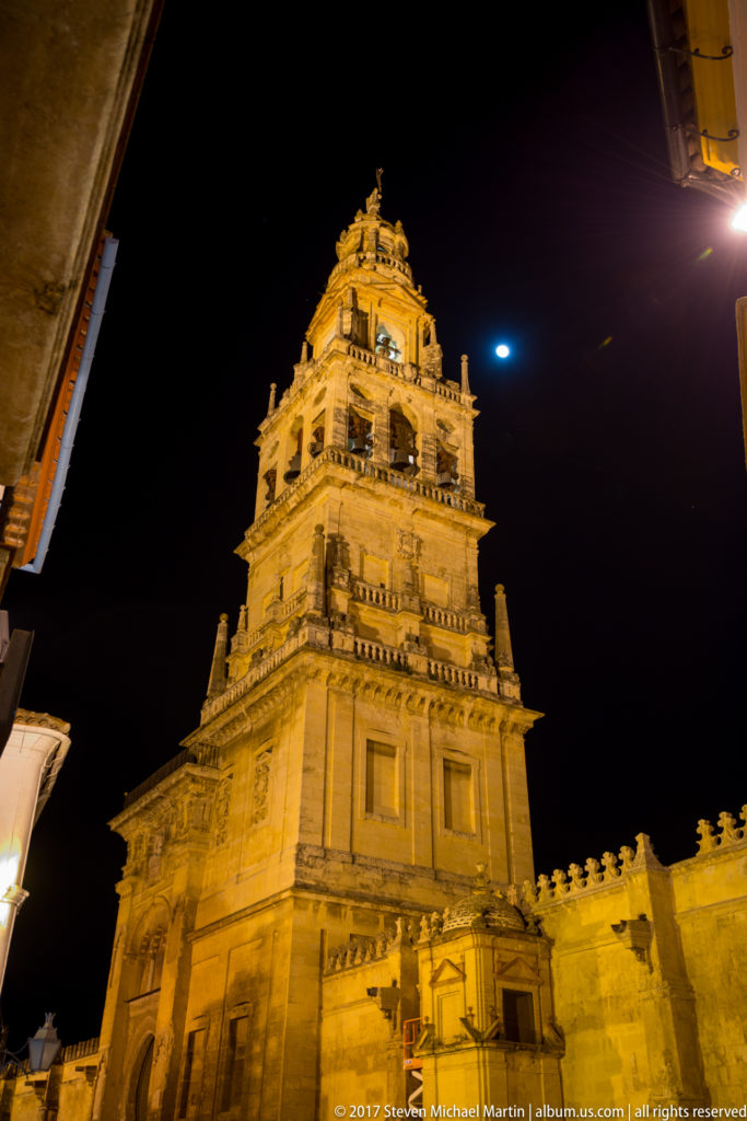 Illuminated bell tower of the Mosque–Cathedral of Córdoba rising into a dark night sky above the surrounding walls.