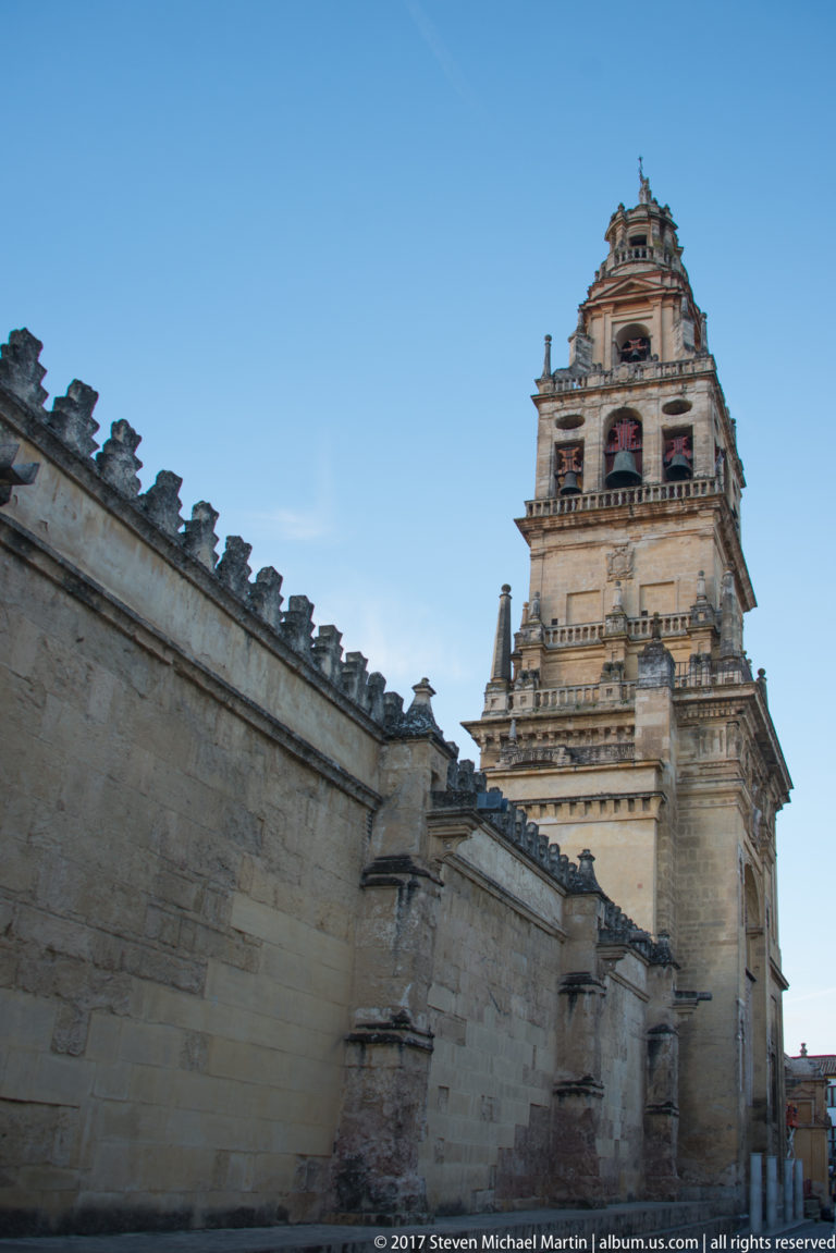Daylight view of the Mezquita bell tower rising behind its crenellated stone perimeter wall.