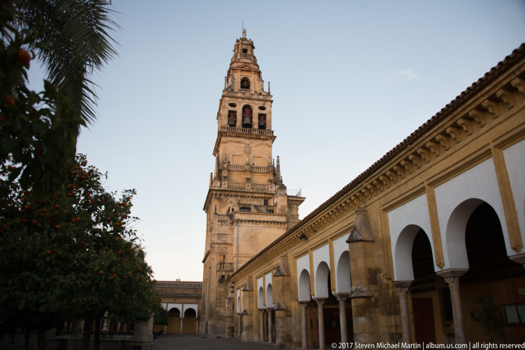 Bell tower seen from the Courtyard of the Orange Trees beside a fruiting orange tree and white arcade.