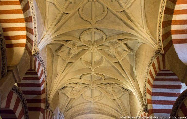 Pale ribbed decorative vault framed on both sides by red-and-light striped arches inside the Mezquita.