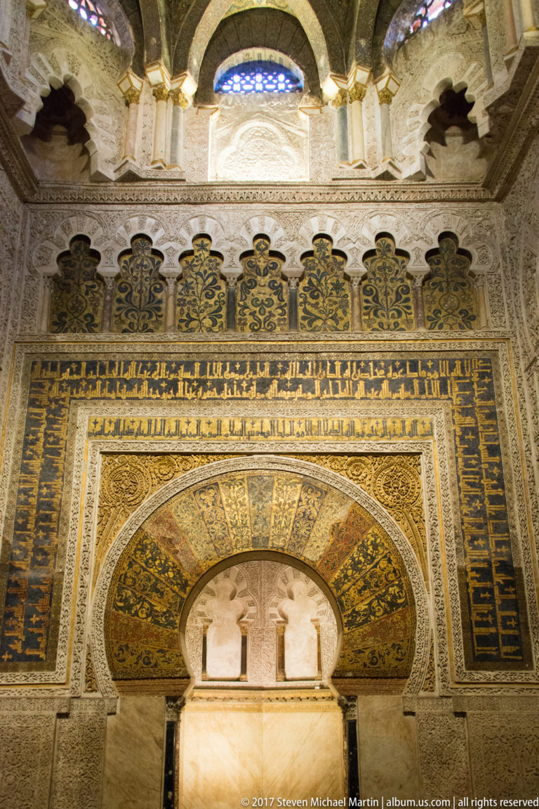 Frontal view of the Mezquita mihrab, with gold mosaics, Arabic inscription bands, and a richly ornamented horseshoe arch.