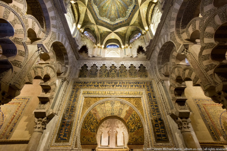 Vertical view of the gold-decorated mihrab, multilobed arches, and ornate domed vault in the Mezquita maqsura.