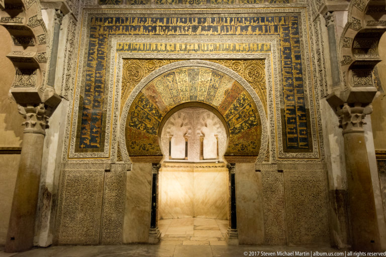 Close frontal view of the Mezquita mihrab with gold mosaic, Arabic inscription bands, and intricate vegetal ornament.