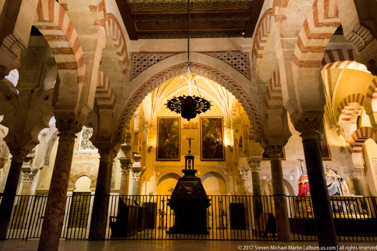 Screened Christian chapel with religious paintings and altar furnishings framed by striped arches inside the Mezquita.