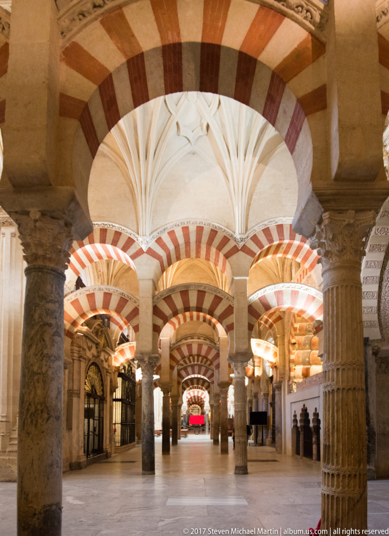 Striped arches and stone columns extend beneath a white ribbed vault inside the Mezquita.