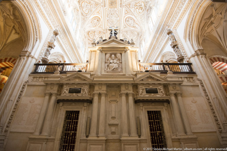 Close upward view of pale cathedral architecture with pilasters, relief panels, balustrade, and ornate white-and-gold vaulting.