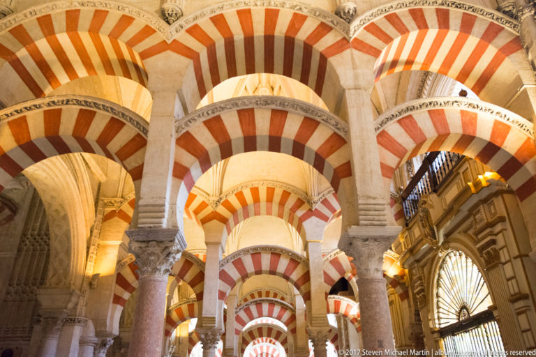 Upward view through layered red-and-light striped arches, columns, and carved capitals in the Mezquita.