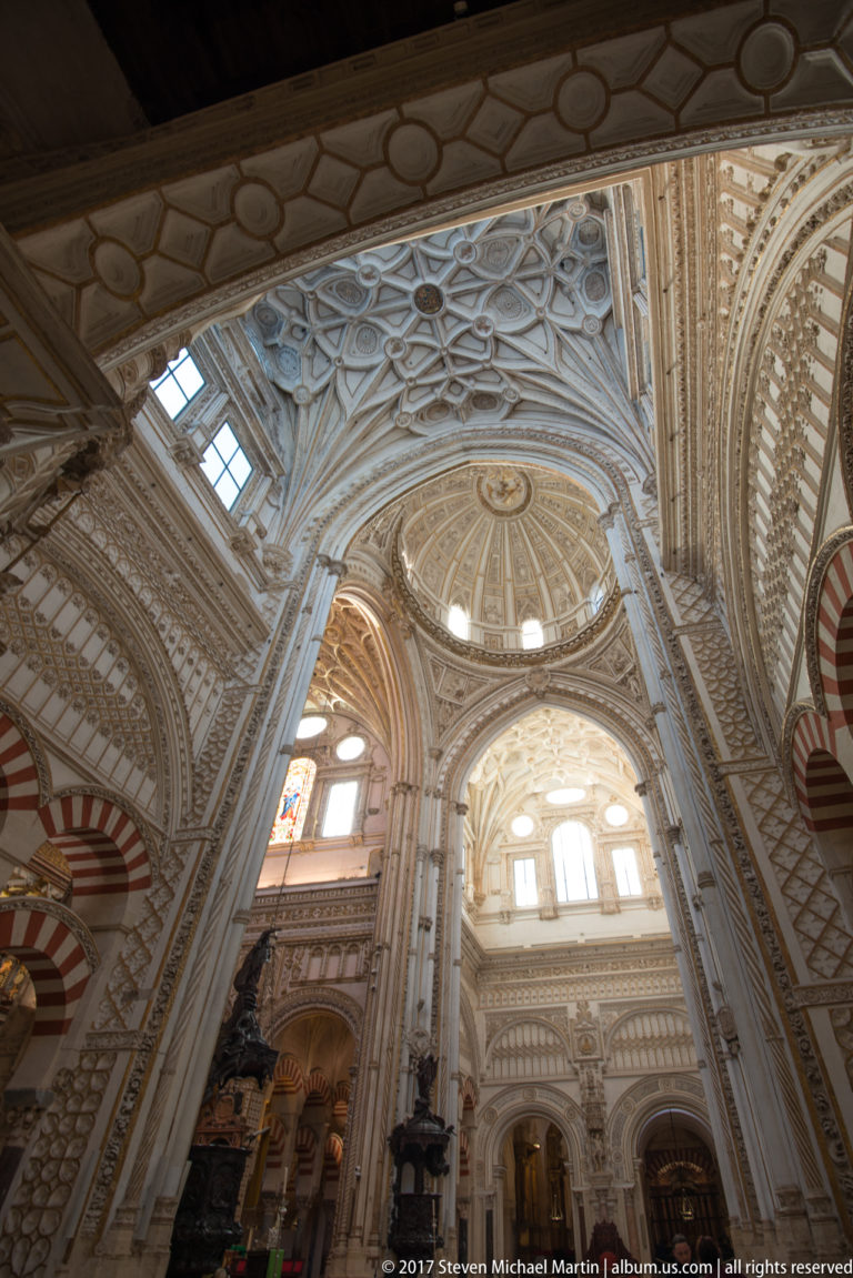 Ornate pale cathedral crossing and dome rising above striped mosque arches inside the Mezquita.