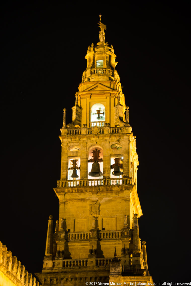 Close frontal night view of the Mezquita bell tower, its arched openings and upper lantern brightly illuminated.