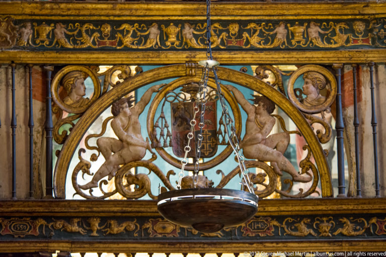 Painted heraldic panel with two lions, central shield, portrait medallions, gold ornament, and a hanging lamp.