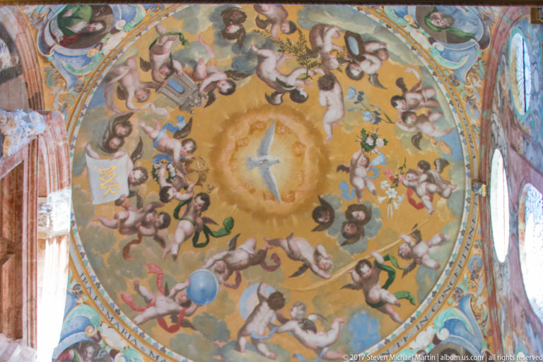Colorful painted dome filled with angels around a luminous central cross, with windows cutting through the surrounding drum.