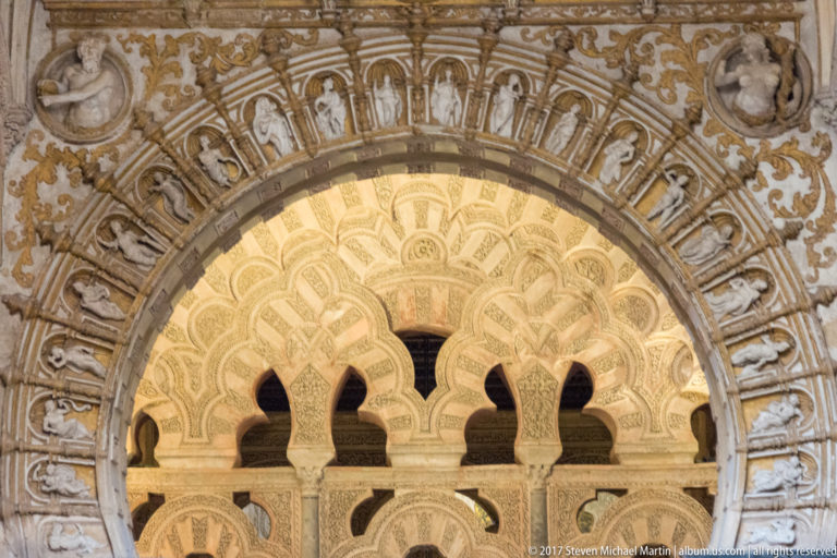 Pale carved multilobed arcade with slender supports and dense relief decoration filling a large arched opening.