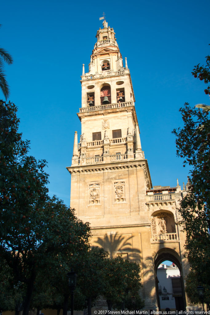 Daylight view of the Mezquita bell tower rising above trees beneath a deep blue sky.