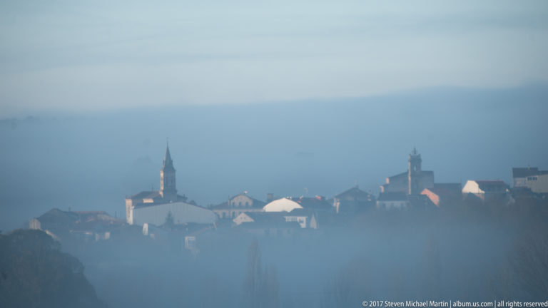 Hilltop village and church tower partly obscured by blue-gray fog.