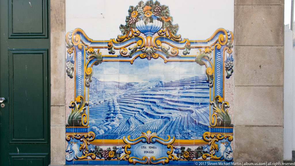 Ornate blue-and-white azulejo panel labeled Uma Vinha Pinhão, showing terraced vineyards within a yellow and blue floral frame.