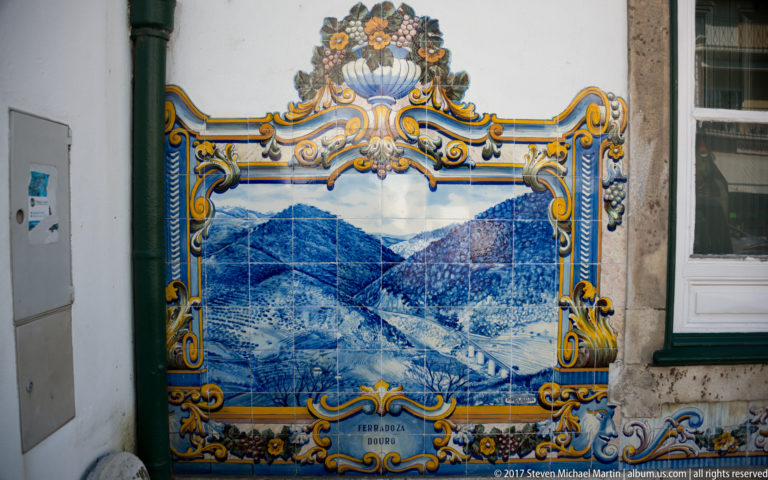 Azulejo panel labeled Rio Douro, with the river winding between steep hills inside an ornate blue and yellow frame.