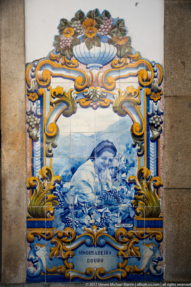 Blue-and-white tile panel of a woman handling harvested grapes, labeled Vindimadeira Douro and surrounded by ornate scrollwork.