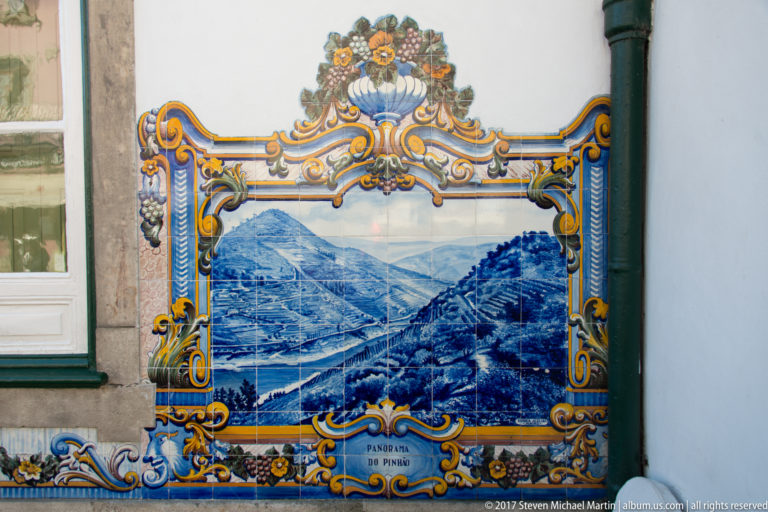 Azulejo panel labeled Panorama do Pinhão, showing a river bend between steep terraced hills beside station doors and stonework.
