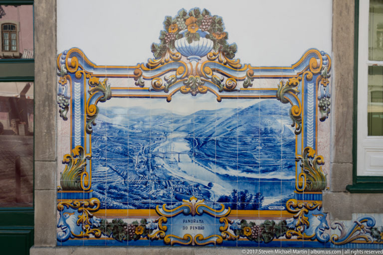 Blue-and-white Panorama do Pinhão azulejo showing the town and a broad Douro River bend from an elevated viewpoint.