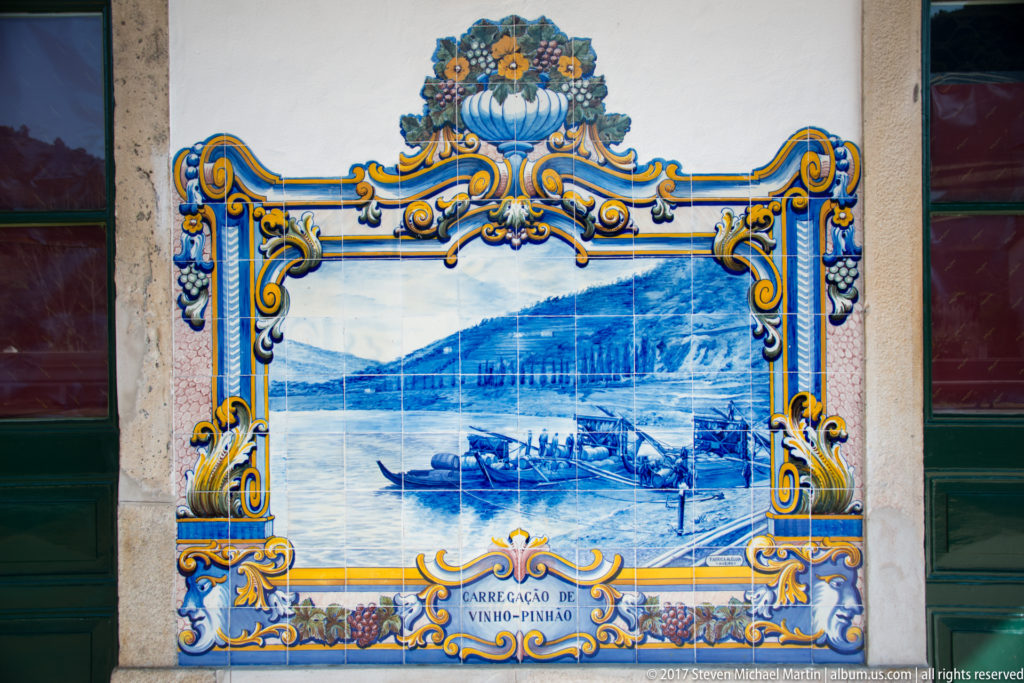 Azulejo panel labeled Carregação de Vinho—Pinhão, showing boats, barrels, and figures loading wine beside the river.