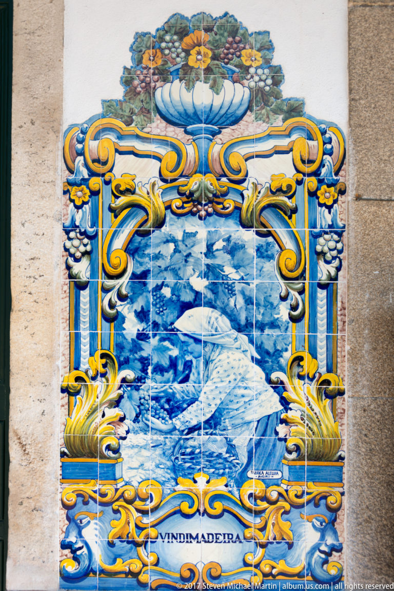 Small azulejo panel labeled Vindimadeira, showing a woman working among grapevines inside an ornate floral frame.