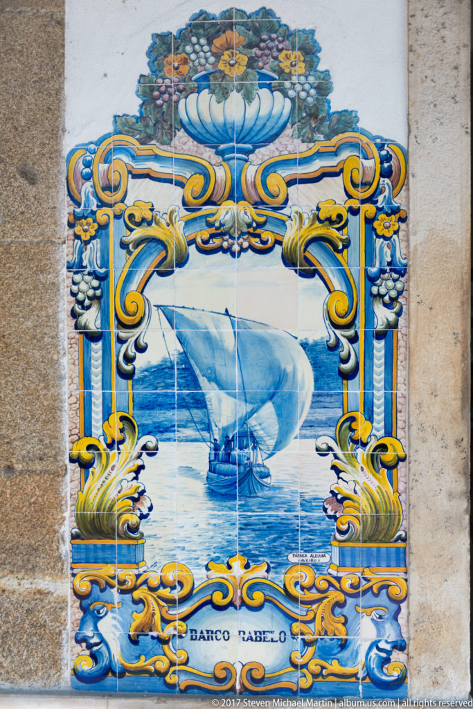 Blue-and-white azulejo labeled Barco Rabelo, showing a traditional Douro cargo boat under a large square sail.