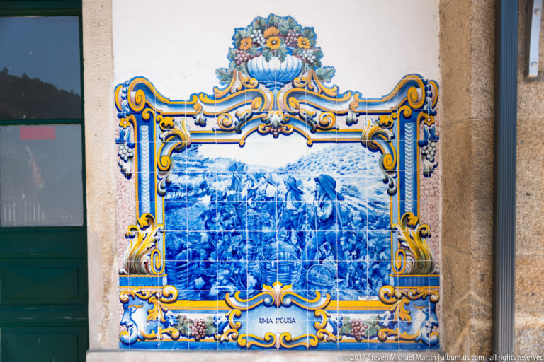 Ornate azulejo panel labeled Uma Pousa, with a dense gathering of people and pack animals in a rural setting.
