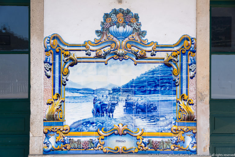 Azulejo panel labeled Pinhão, showing boats and riverside activity below steep hills within an ornate frame.