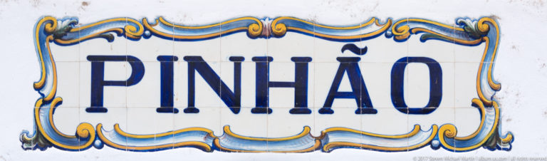 Glazed ceramic sign reading “PINHÃO” in blue letters within an ornate blue-and-gold border.