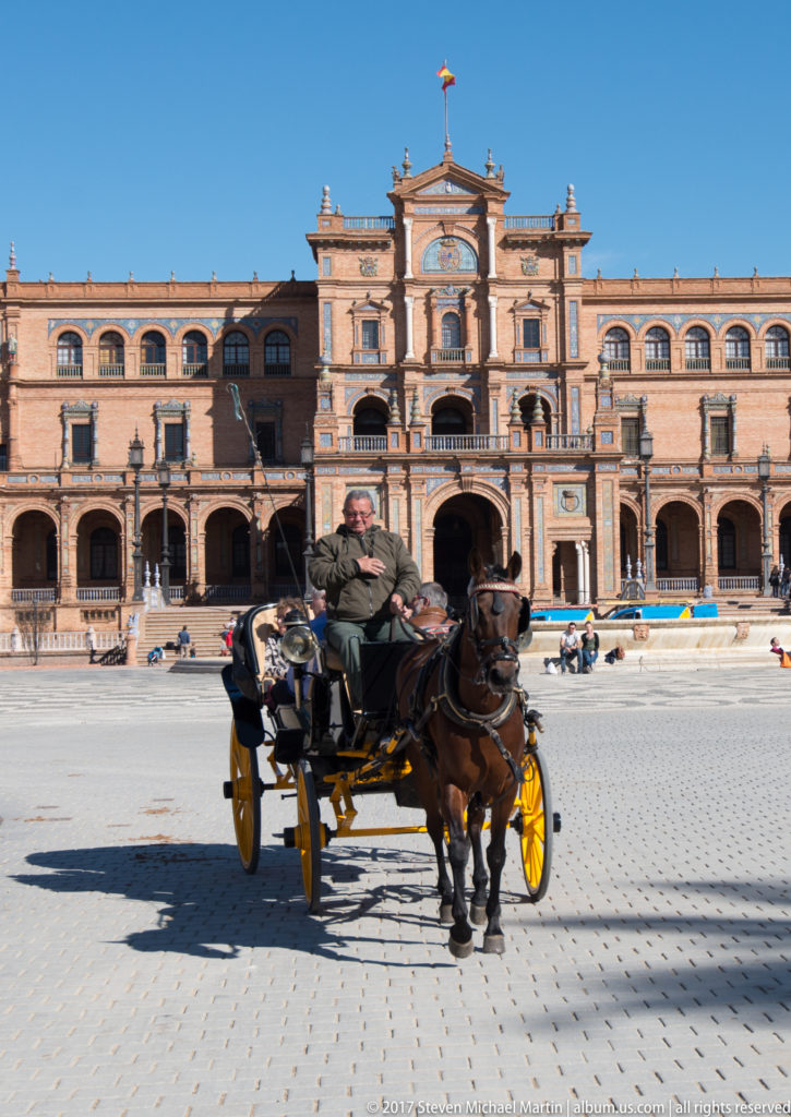 Horse-drawn carriage with two horses crossing Plaza de España before its arcaded central pavilion in Seville.