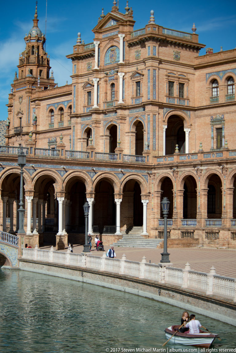 Brick pavilion with arcaded lower level stands beside the canal at Plaza de España, viewed closely across the water.