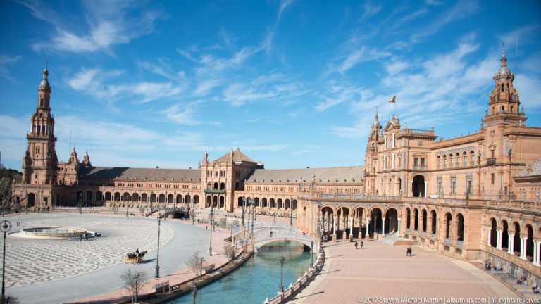 Elevated wide view across Plaza de España showing canal, bridge, central pavilion, arcades, and twin towers.