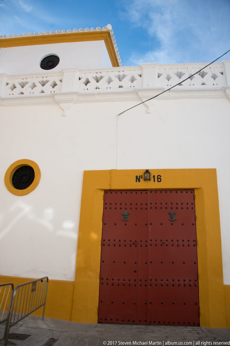 White and ochre bullring wall with red studded door marked number 16 and a small oval window.