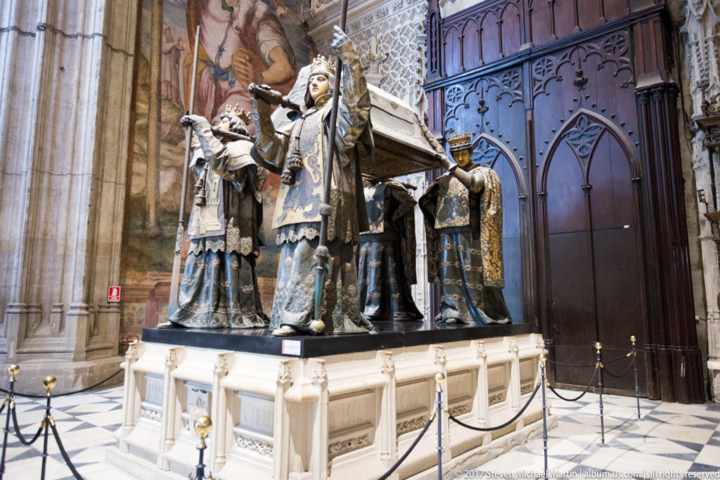 Four crowned heraldic figures carry the sarcophagus of Christopher Columbus on a white pedestal inside Seville Cathedral.