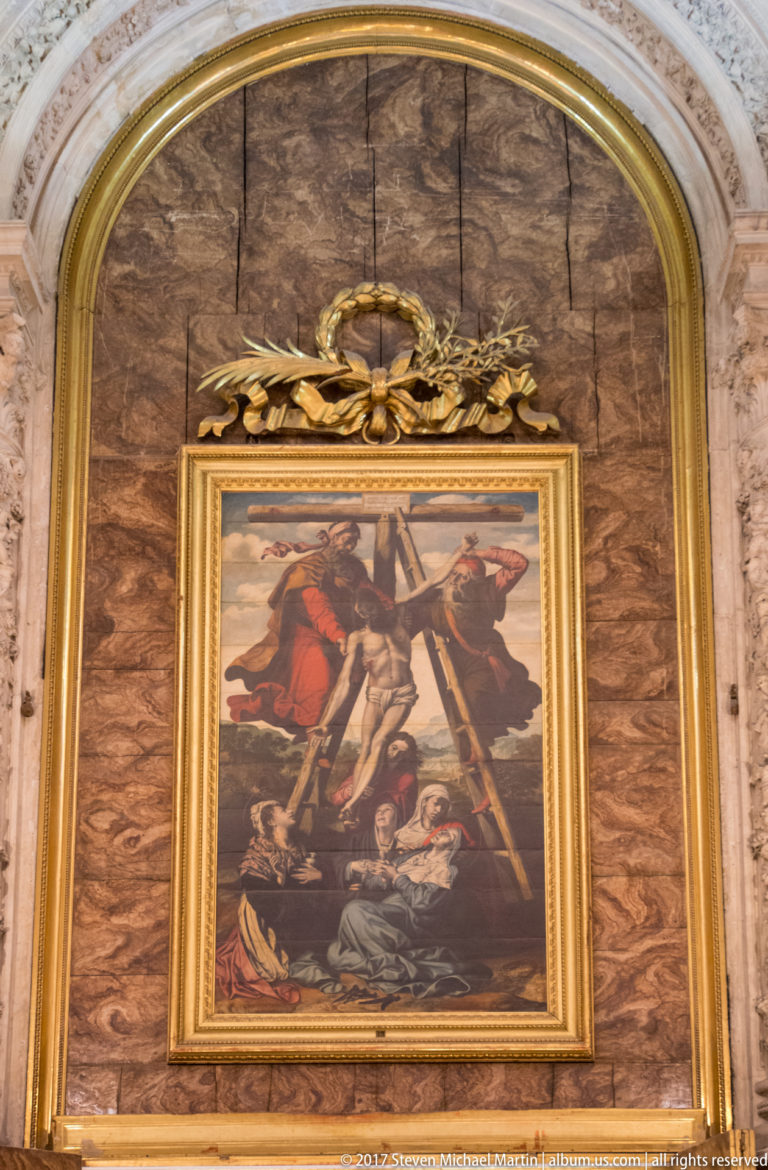 Framed religious painting of several figures around a fallen body, set in a red-veined arched niche with gilded ornament.