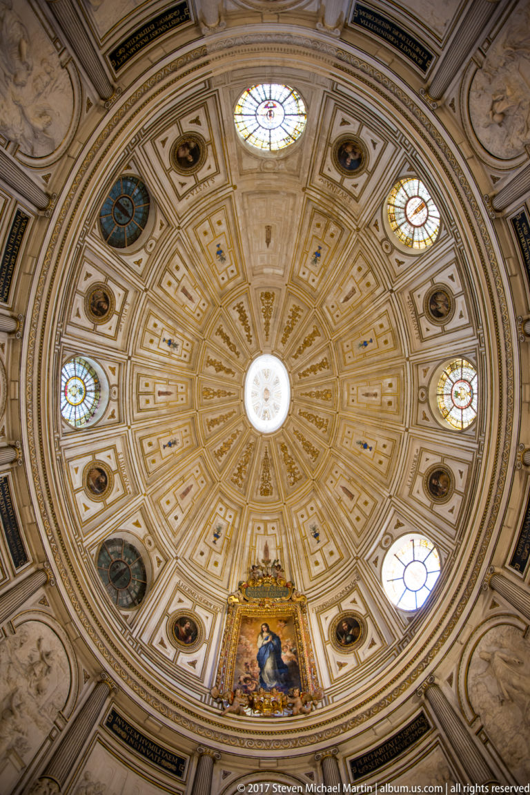 Radial gilded coffered dome with central oculus, small stained-glass windows, painted medallions, and devotional image below.