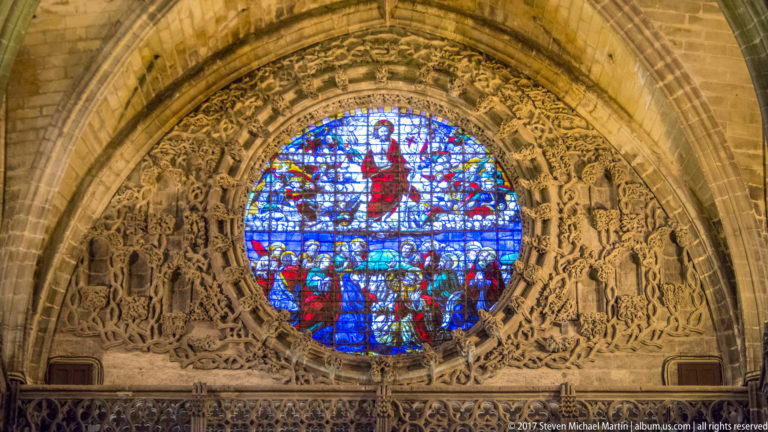 Circular blue-and-red stained-glass window surrounded by richly carved stone figures and tracery in the cathedral.