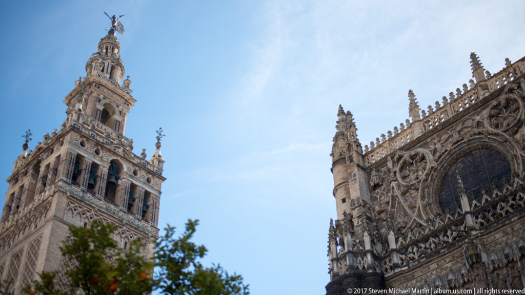 Giralda tower beside ornate Gothic cathedral façade with pinnacles, tracery, and a large dark window.