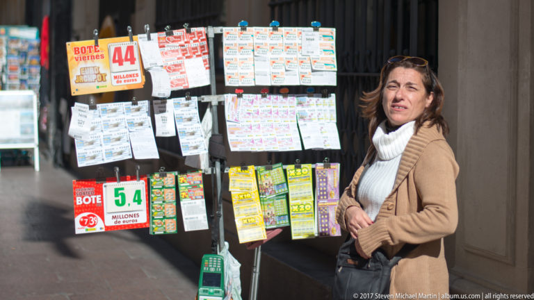 Woman stands beside a street kiosk densely covered with lottery tickets and promotional cards in Seville.