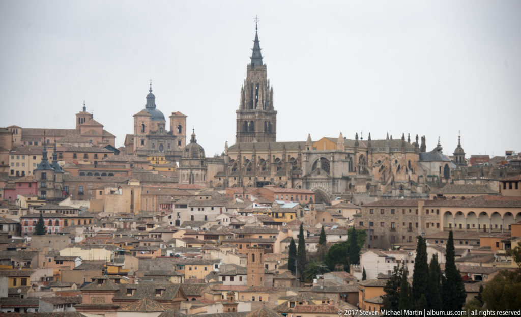 Historic Toledo skyline with clustered roofs, church domes, and the Gothic tower of Toledo Cathedral rising above the city.